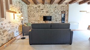 Una sala de estar con pared de piedra, un sofá gris, un televisor montado en la pared y un radiador.