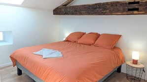 Un dormitorio con techo inclinado, una cama con colcha naranja, una lámpara de noche y un tragaluz.