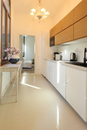 A modern kitchen with white cabinetry, a chandelier, and a vase of flowers on the counter. - Venice 2 Green (Venezia)