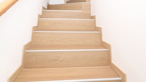 Eine Holztreppe mit Handlauf, die zu einer Zwischenebene mit einem Holzbalken führt.
