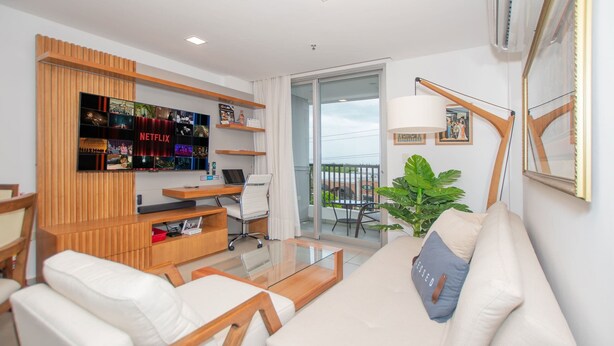 A modern living room with a sofa, chairs, a coffee table, a TV with Netflix branding, a laptop, and a balcony with a plant. - Corporate Stays Centric Felix Bogado (Asunción)