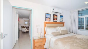 A hotel room with a bed, bedside table, lamp, and wall-mounted air conditioner. There are framed pictures on the wall and a window with curtains. - Corporate Stays Centric Felix Bogado (Asunción)