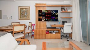 A modern living room with a wooden entertainment unit, a sofa, a glass coffee table, and a dining area with chairs. - Corporate Stays Centric Felix Bogado (Asunción)