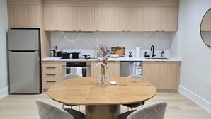 Eine moderne Küche mit Holzschränken, einem Edelstahlkühlschrank, einem runden Esstisch mit Stühlen und einem eingebauten Backofen.
