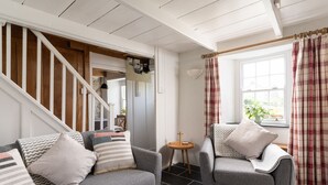 Ein Wohnzimmer mit grauem Sofa, grauem Sessel, kleinem runden Tisch, einer Treppe und einem Fenster mit Vorhängen.