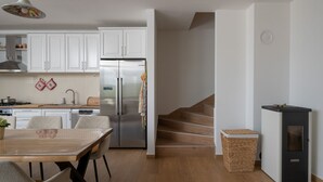 Una cocina moderna con armarios blancos, un refrigerador de acero inoxidable, una mesa de comedor con sillas y una escalera de madera.