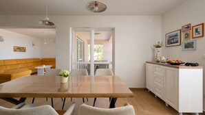 Un comedor moderno con una mesa de madera, sillas blancas, un armario blanco y vistas a través de un ventanal.