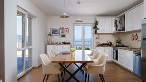 Una cocina moderna con armarios blancos, una mesa de comedor con cuatro sillas y vistas a través de puertas de vidrio.