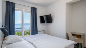 Un cuarto de hotel con cama, televisión, una silla y vista al mar.