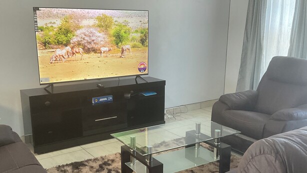A living room with a flat-screen TV on a stand, a glass coffee table, and two grey sofas.