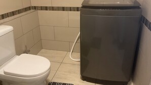 A bathroom with a toilet, a trash bin, and a shower area.