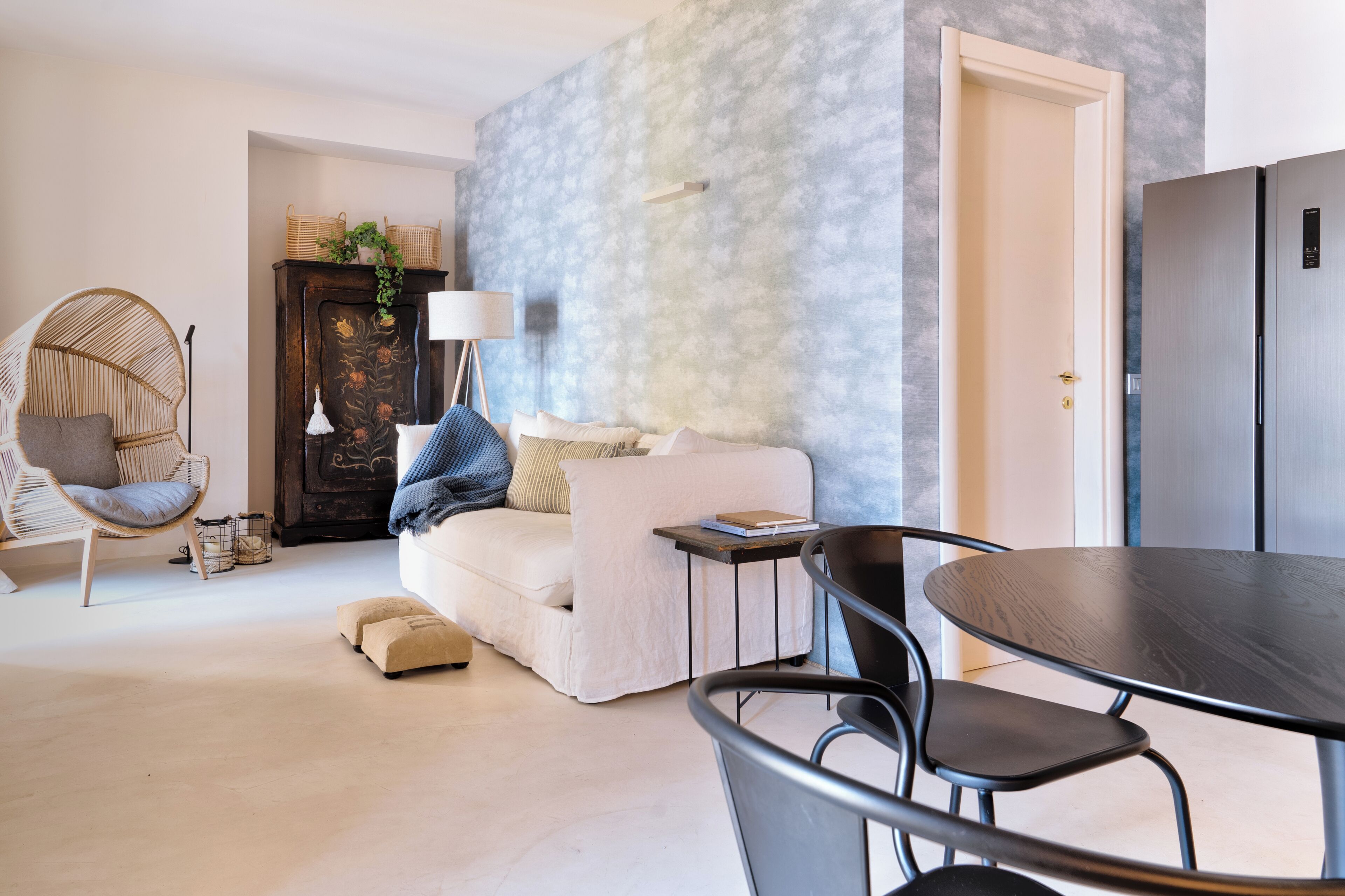 Un salon comprenant un canapé, une table à manger, des chaises, une lampe, un fauteuil en osier et un buffet.