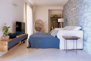 Ein modernes Schlafzimmer mit Bett, Fernseher auf einem Regal, einem Sessel und einem kleinen Tisch.