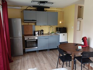 A compact kitchen with a refrigerator, oven, microwave, and sink. There is a dining table with chairs and a red coffee machine.