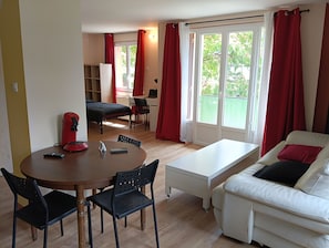 A room with a bed, a desk, a dining table with chairs, a sofa, and a window with curtains.