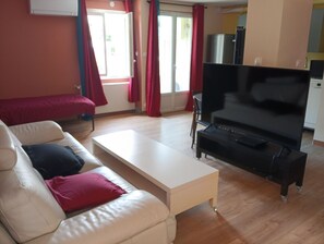 A living room with a sofa, a coffee table, a TV, and a kitchen area in the background.