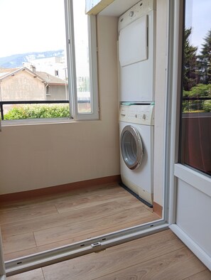Un lavadero con lavadora, una ventana y vistas de edificios al exterior.
