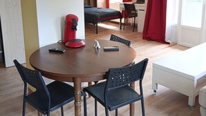 A room with a round wooden table, four chairs, a bed, a desk, and a window with red curtains. - New, very comfortable 47 m² loft between Vercors and the foothills of the Chartreuse (Saint-Martin-le-Vinoux)