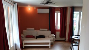 A living room with a sofa, a dining table, and a window with curtains. - New, very comfortable 47 m² loft between Vercors and the foothills of the Chartreuse (Saint-Martin-le-Vinoux)