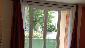 A room with a wooden floor, a sliding glass door with curtains, and a view of greenery outside. - New, very comfortable 47 m² loft between Vercors and the foothills of the Chartreuse (Saint-Martin-le-Vinoux)