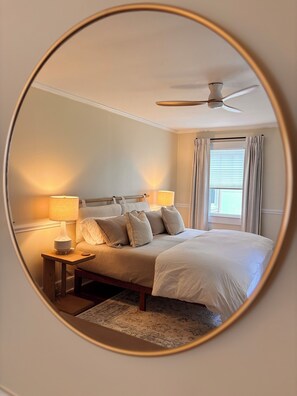 A bedroom with a bed, two bedside lamps, a ceiling fan, and a window with curtains.