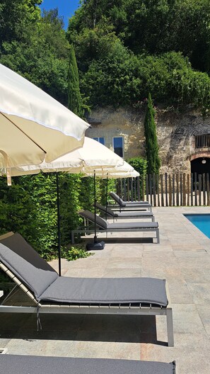 A poolside area with lounge chairs and umbrellas, surrounded by greenery and stone walls. - Apartment with pool near Amboise | Sleeps 4 + 1 baby (Pocé-sur-Cisse)