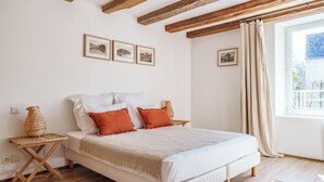 Ein Bett mit weißer Bettwäsche und orangefarbenen Kissen, Nachttische aus Holz, ein gewebter Korb und gerahmte Bilder an der Wand.