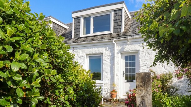 A white cottage with a stone pathway leading to the door, surrounded by lush greenery. - 4 Whiterow (Appin)