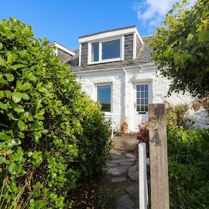 Ein weißes Cottage mit einem Kiesweg, der zur Tür führt, umgeben von üppigem Grün.