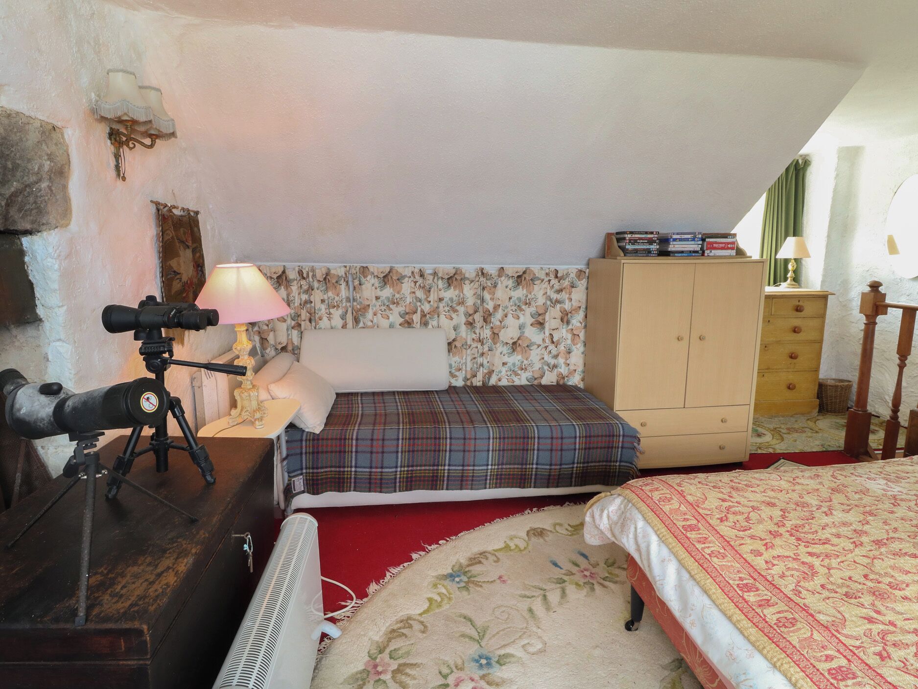 A bedroom with a bed, a small table with a lamp, a wardrobe, and a telescope on a tripod.