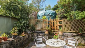 A stone wall, two metal chairs, a round metal table, and potted plants in a garden area. - 4 Whiterow (Appin)