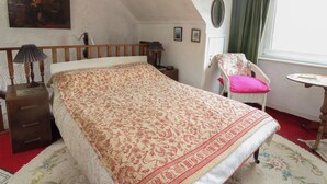 A bedroom with a bed, a chair, a small table, a lamp, a painting, and a window with curtains. - 4 Whiterow (Appin)