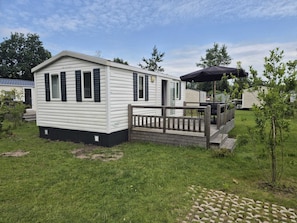Een stacaravan met een terras, een klein portaal en een barbecueplek.