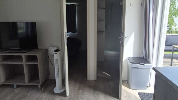 Una habitación moderna con televisión de pantalla plana, calefactor portátil, un cesto de basura y una puerta corredera de vidrio que da a un área exterior.