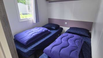 Ein kleines Zimmer mit zwei Betten, einem fensterbelaubten Fenster und einer eingebauten Ablage über den Betten.