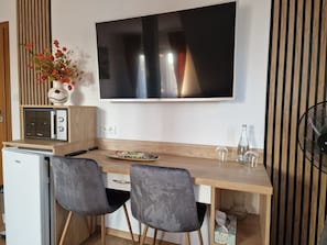 A modern kitchenette with a flat-screen TV, a microwave, and a small refrigerator. There are two grey chairs and a wooden table with a decorative plate and glassware. - Baltic Sand - Osrodek Wypoczynkowy (Władysławowo)