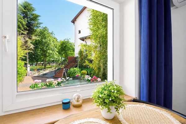 A room with a large window, a potted plant, a small table, and a blue curtain.