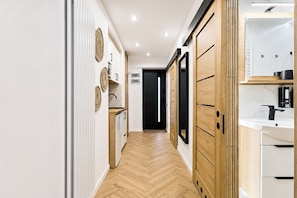 A hallway with wooden flooring, a white wall with decorative plates, and a black door at the end.