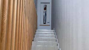 Una escalera con paneles de madera en un lado y una pared lisa en el otro, que conduce a una puerta con un cuadro enmarcado.