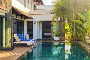 Uma área à beira da piscina com espreguiçadeira, cama e planta em vaso.