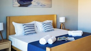 Una habitación de hotel con una cama, almohadas, una mesita de noche, una lámpara, una toalla y un folleto.