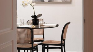 En matplats med ett runt bord, två fåtöljer i rotting, en vas med en orkidé och en modern lampa ovanför.