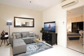 A modern living room with a sectional sofa, a flat-screen TV, a coffee table, and a large mirror. - New! Modern Chic 2BR Condo with Fast Wifi (Makati)
