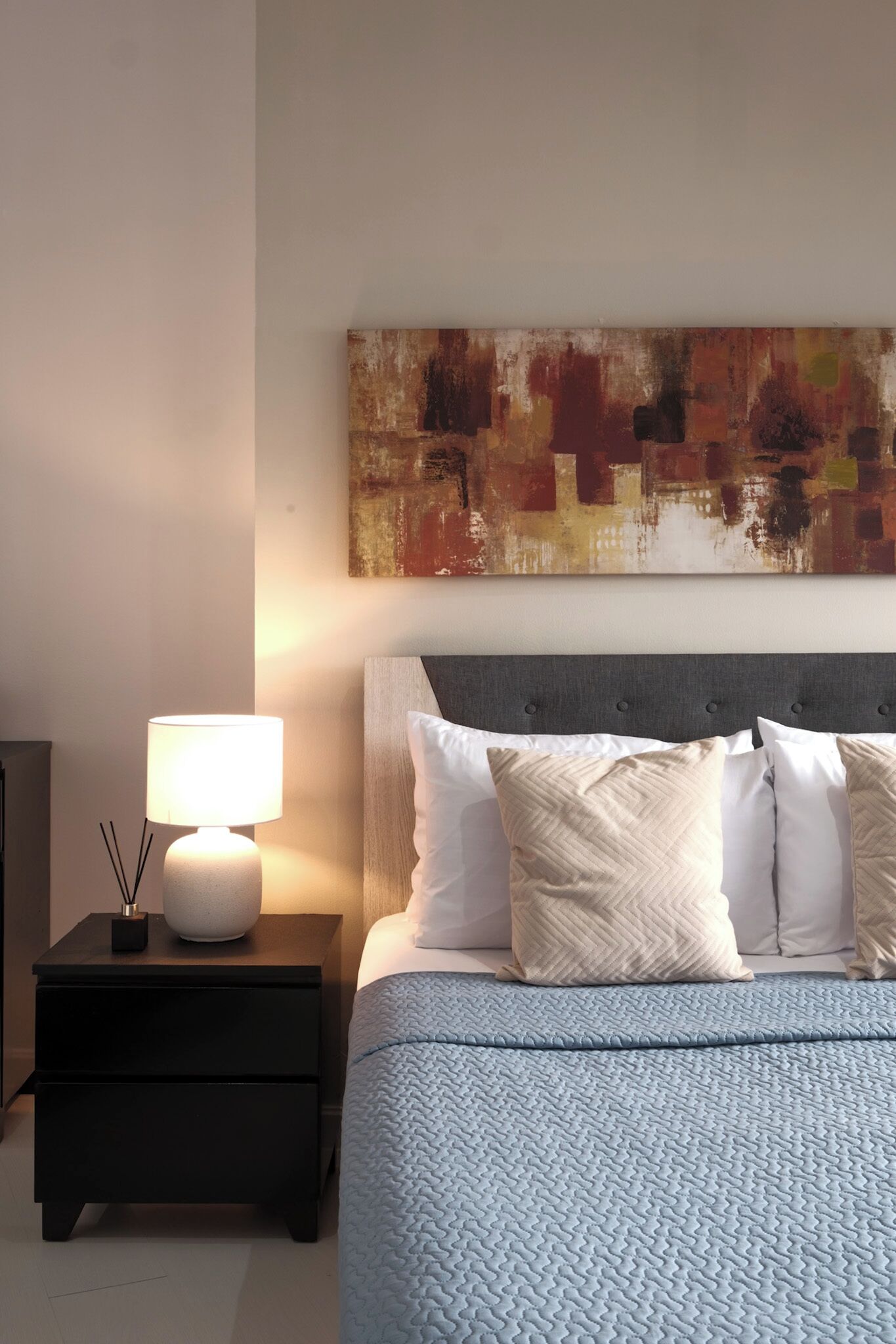 Een slaapkamer met een bed, nachtkastje, lamp en abstract kunstwerk aan de muur.