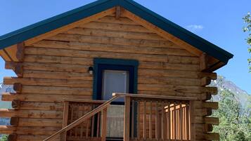 Une cabane en rondins avec un escalier en bois menant à un balcon, une porte et une fenêtre.