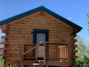 A log cabin with a wooden staircase leading to a balcony, a door, and a window. - Scenic Creekside Cabin with Panoramic Bay & Mountain Views in Seward, Alaska (Seward)