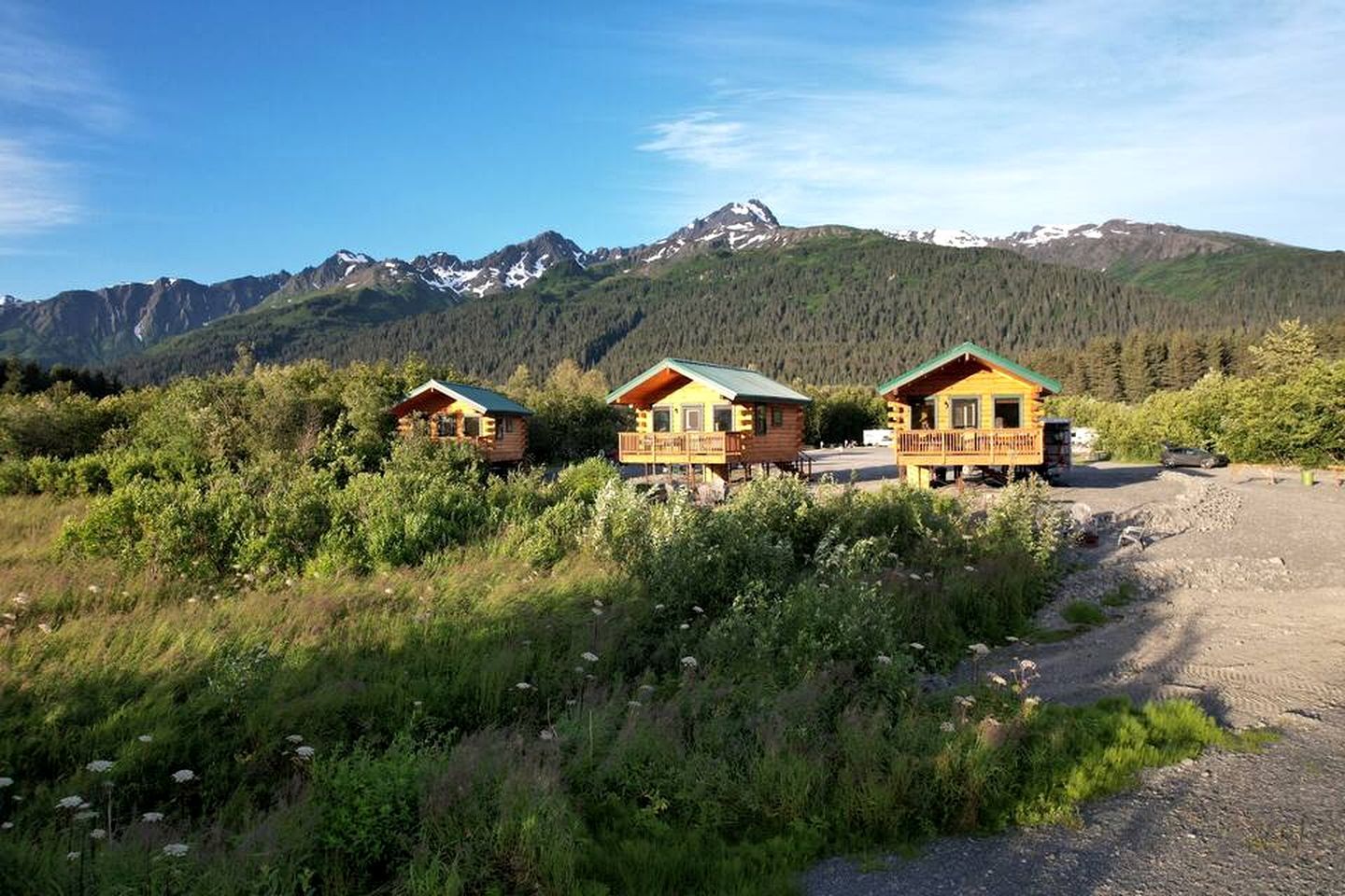 Trois chalets en bois dotés de balcons, entourés de verdure et avec des montagnes en toile de fond.