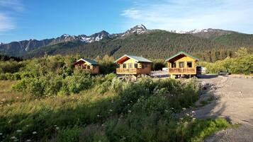 Trois chalets en bois dotés de balcons, entourés de verdure et avec des montagnes en toile de fond.
