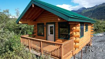 A wooden cabin with a green roof, a front door, and a balcony.