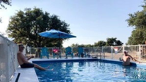 Ein Schwimmbecken mit einem Metallzaun, einem blauen Sonnenschirm und einigen Stühlen.